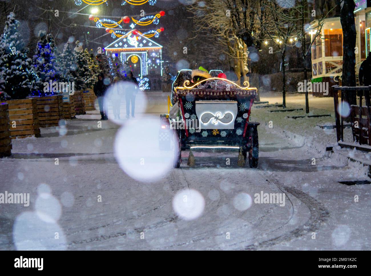 Un wagon joliment décoré qui descend dans une rue enneigée pendant les fortes chutes de neige les soirs d'hiver. Back-end Beaucoup d'arbres de Noël, décorations décoratives, illuminations et lumières de rue. Noël du nouvel an Banque D'Images