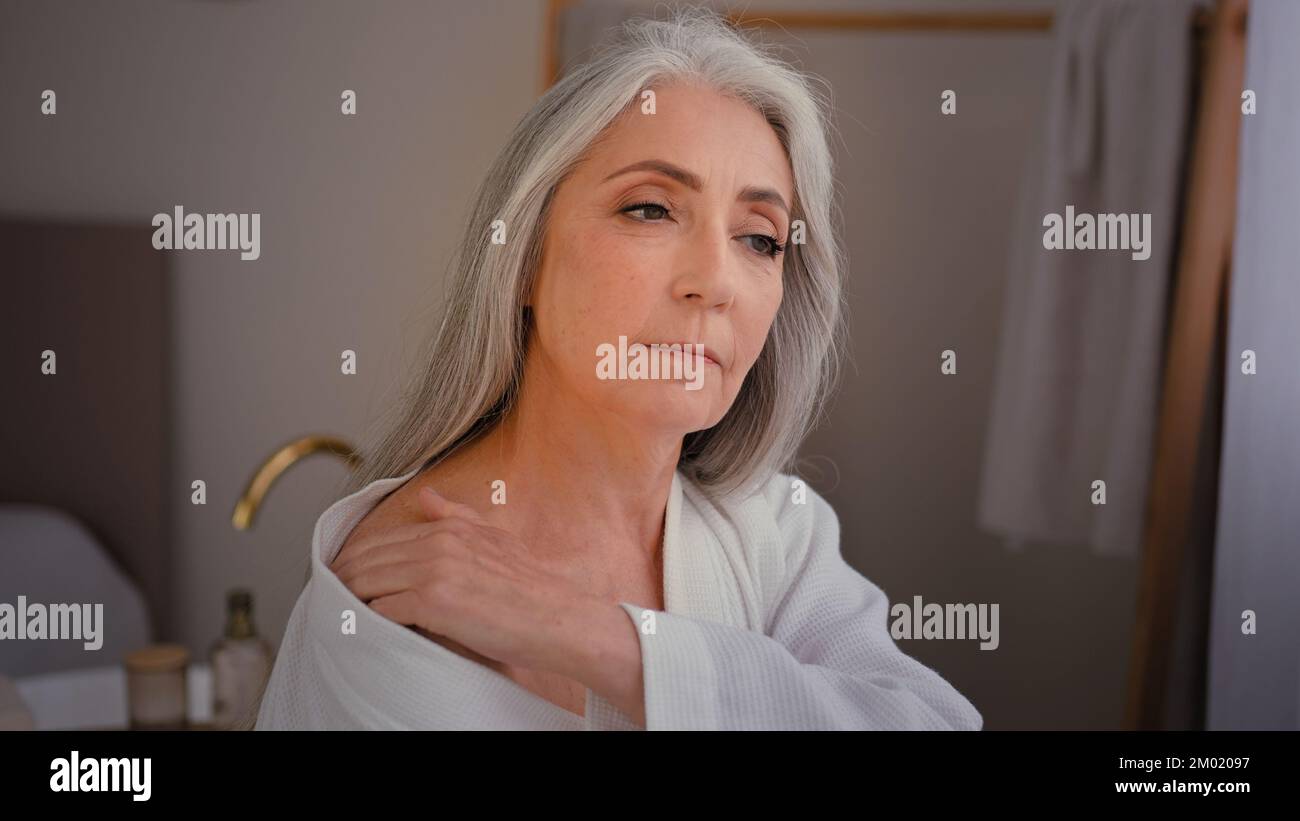 Caucasien granny grand-mère ancien modèle femme âgée 60s Femme caucasienne femme en peignoir dans la salle de bains frottis épaules dos et cou poitrine avec Banque D'Images