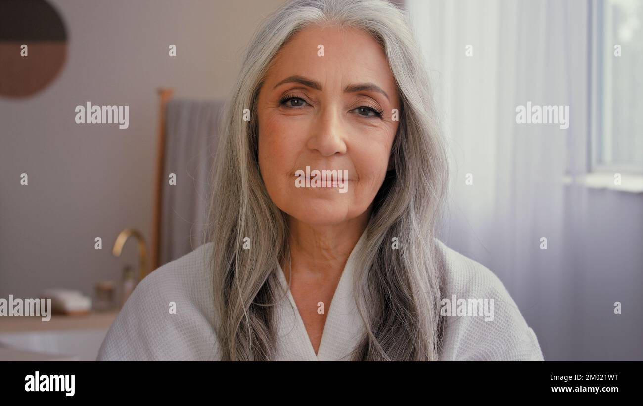 Portrait à l'intérieur vieux caucasien 50s senior modèle gris-cheveux mature femme 60s dame dans la salle de bains montrant pot de l'anti-âge cosmétique naturel organique Banque D'Images