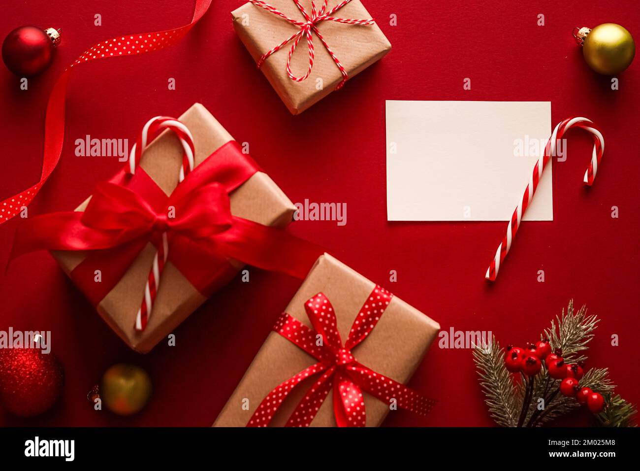 Décorations de Noël, cadeaux et décoration avec carte de vœux blanche vierge ou carte de visite ou de remerciement sur fond rouge festif comme placolatte de fêtes. Banque D'Images