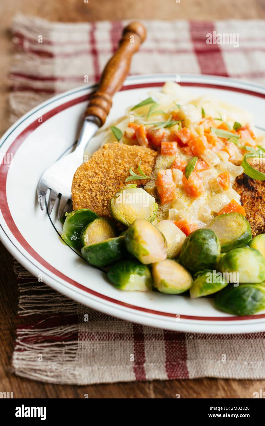 Schnitzel aux légumes sur des nouilles avec une sauce crémeuse à l'estragon et des choux de Bruxelles. Banque D'Images