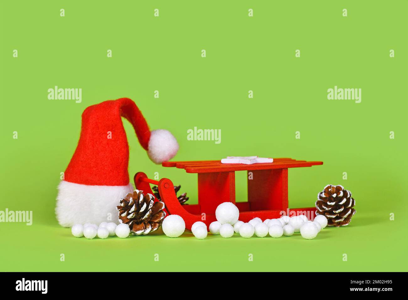 Décoration de Noël de saison avec toboggan miniature, cônes de sapin, chapeau de père noël et boules de neige sur fond vert Banque D'Images