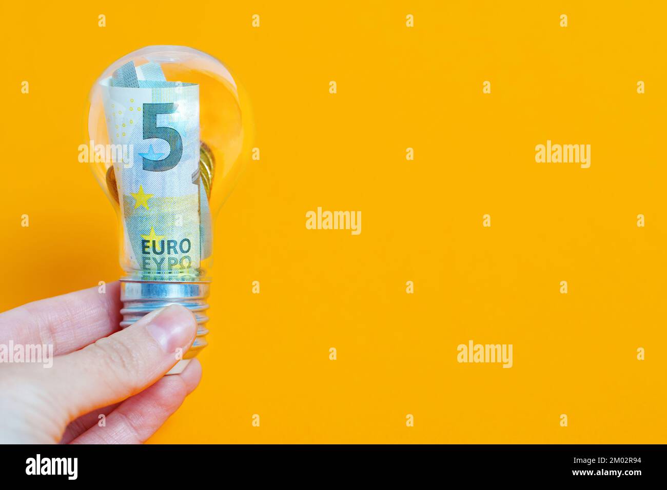 Billet de banque et pièces de monnaie en euros placés à l'intérieur d'une ampoule isolée sur fond jaune. Concept d'idée commerciale rentable. Banque D'Images