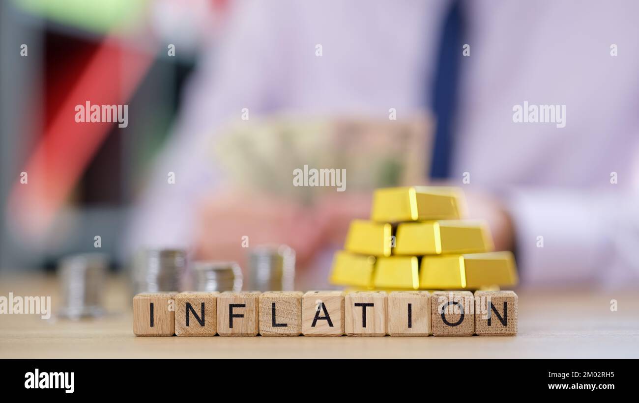 L'inflation des mots collectée à partir de cubes et de pièces floues, l'or et l'homme d'affaires comptant l'argent en arrière-plan. Banque D'Images