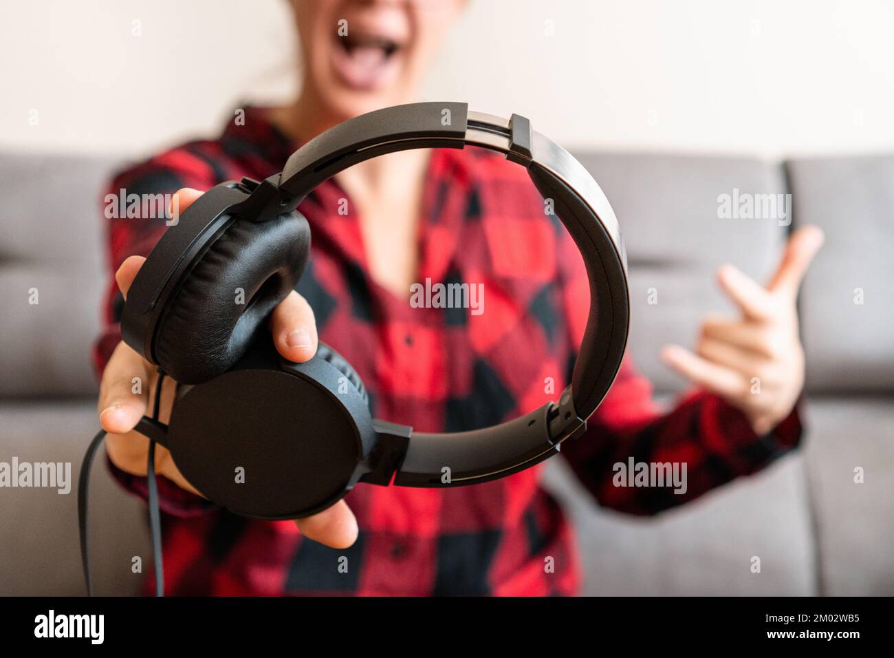 Personne offrant avec enthousiasme des écouteurs filaires noirs vers la caméra à la maison. Concept de style de vie ludique de musique et divertissement audio. Banque D'Images