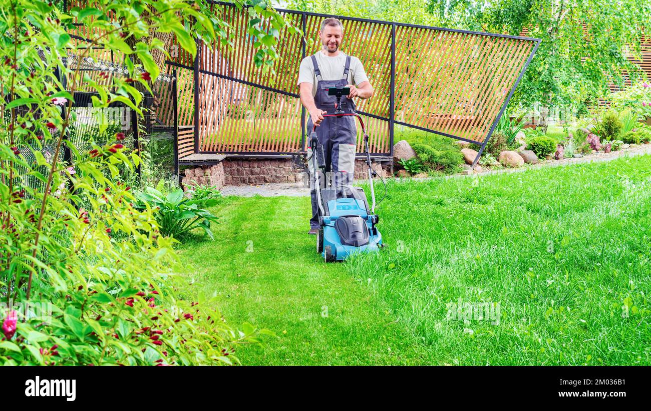 Le jardinier s'occupe de la pelouse en fauchant l'herbe à l'aide d'une tondeuse électrique. Un homme surfe sur Internet et s'engage dans le commerce en ligne pendant le cho Banque D'Images