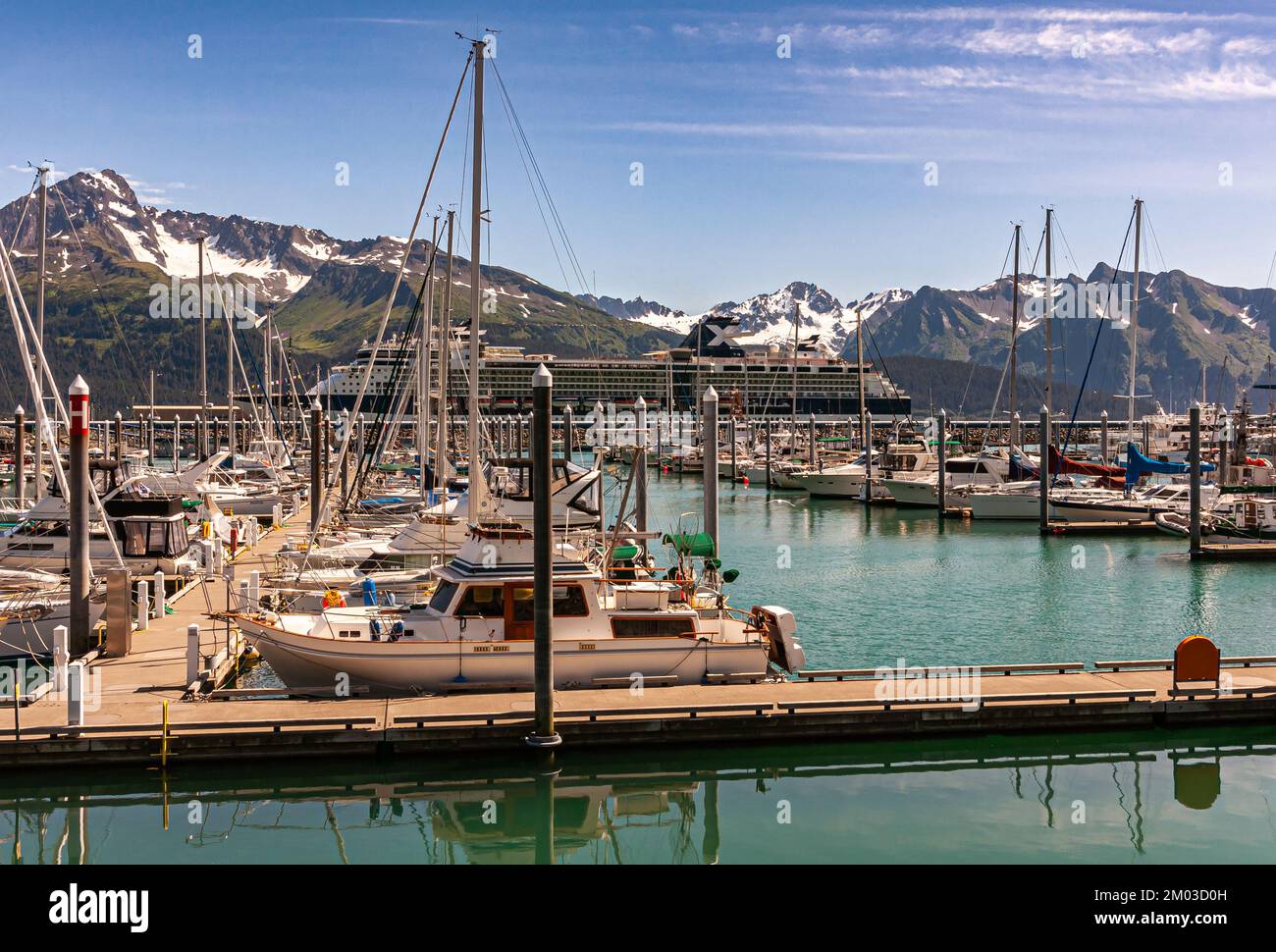Seward, Alaska, Etats-Unis - 22 juillet 2011: Célèbre navire de croisière du millénaire derrière petit bateau piers sur l'eau verdâtre de la baie de Résurrection. Chaîne de montagnes avec Banque D'Images