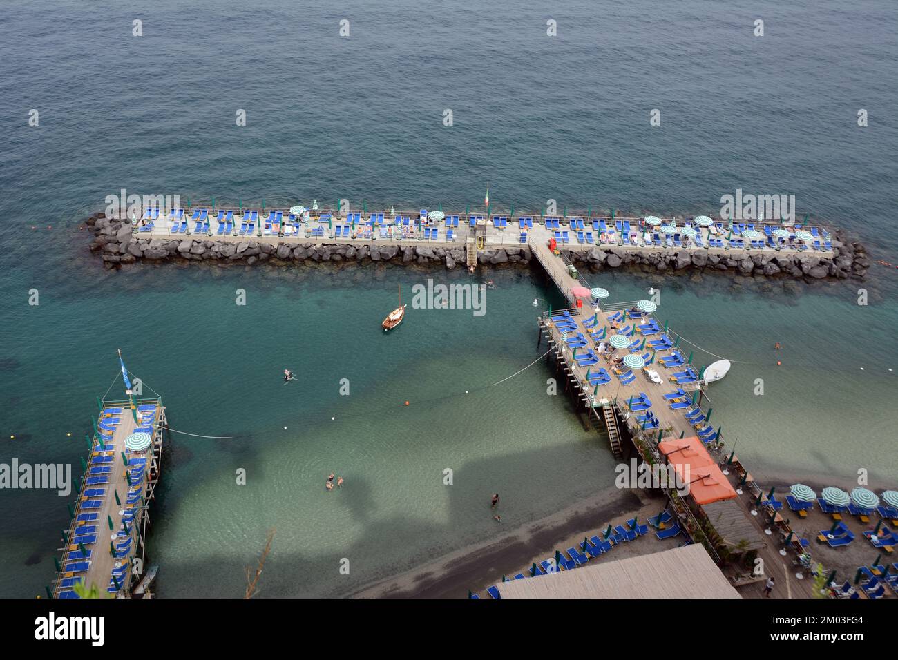 Une terrasse privée de club de plage avec chaise, parasols et nageurs, dans la mer Méditerranée, sous les falaises de Sorrento, Campanie, Italie. Banque D'Images