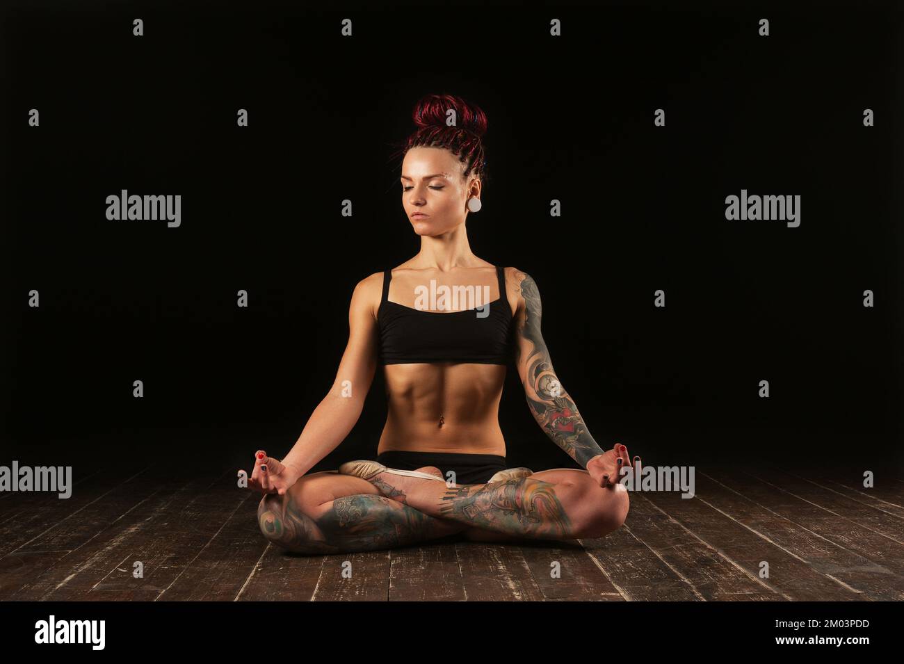 Fitness jeune femme athlète pratiquant le yoga méditant en position lotus sur fond noir Banque D'Images