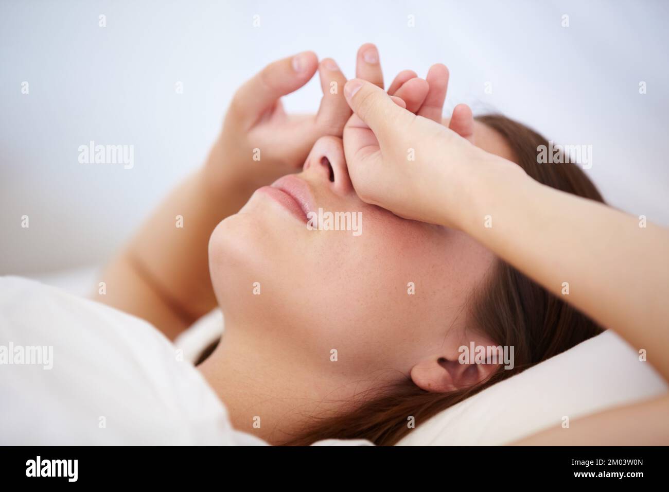 Se réveiller avec un énorme mal de tête. Une jeune femme couché au lit avec ses mains au-dessus de ses yeux. Banque D'Images