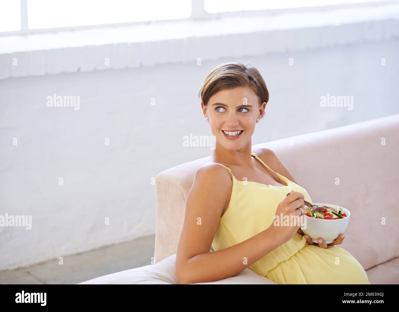 Rester en bonne santé, rester heureux. une belle femme enceinte se détendant sur le canapé tout en mangeant une salade fraîche. Banque D'Images