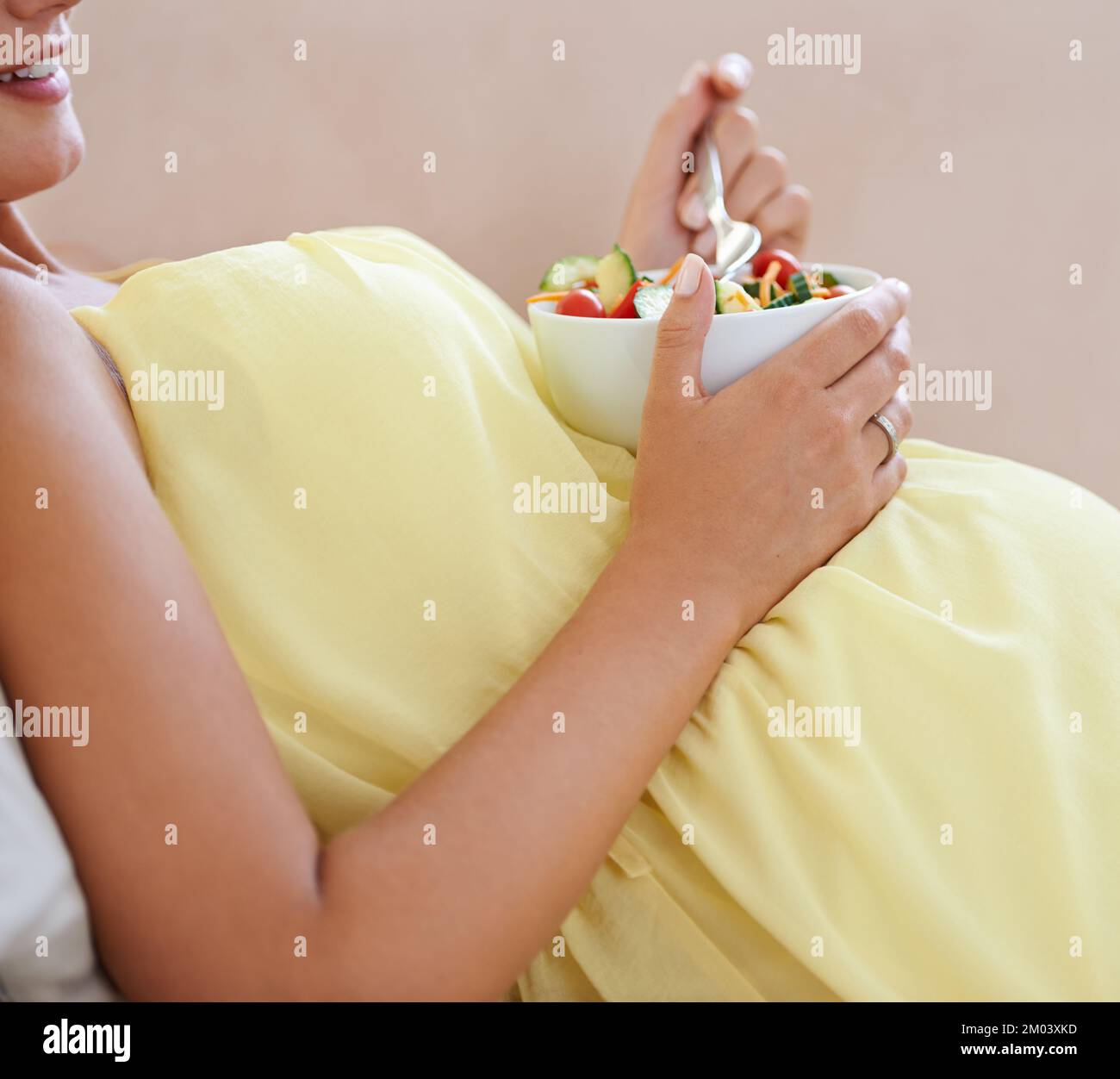 Grossesse en bonne santé, grossesse heureuse. une femme enceinte se détendant sur le canapé tout en mangeant une salade fraîche. Banque D'Images