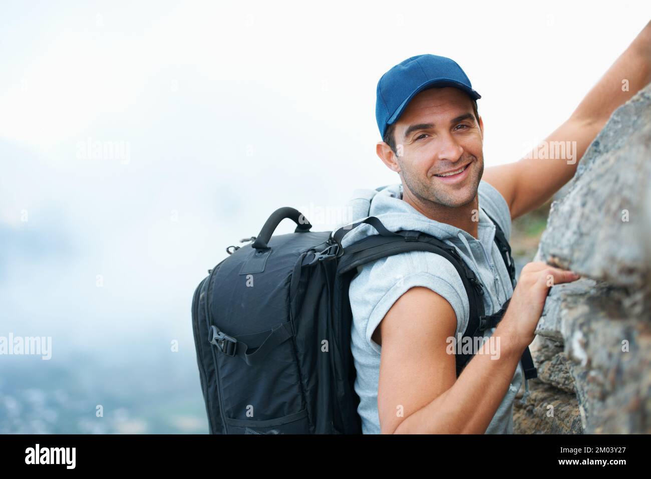 Il n'y a aucune limite pour ce chercheur de sensations fortes. Jeune grimpeur souriant à la caméra alors qu'il balance le sommet d'une falaise. Banque D'Images