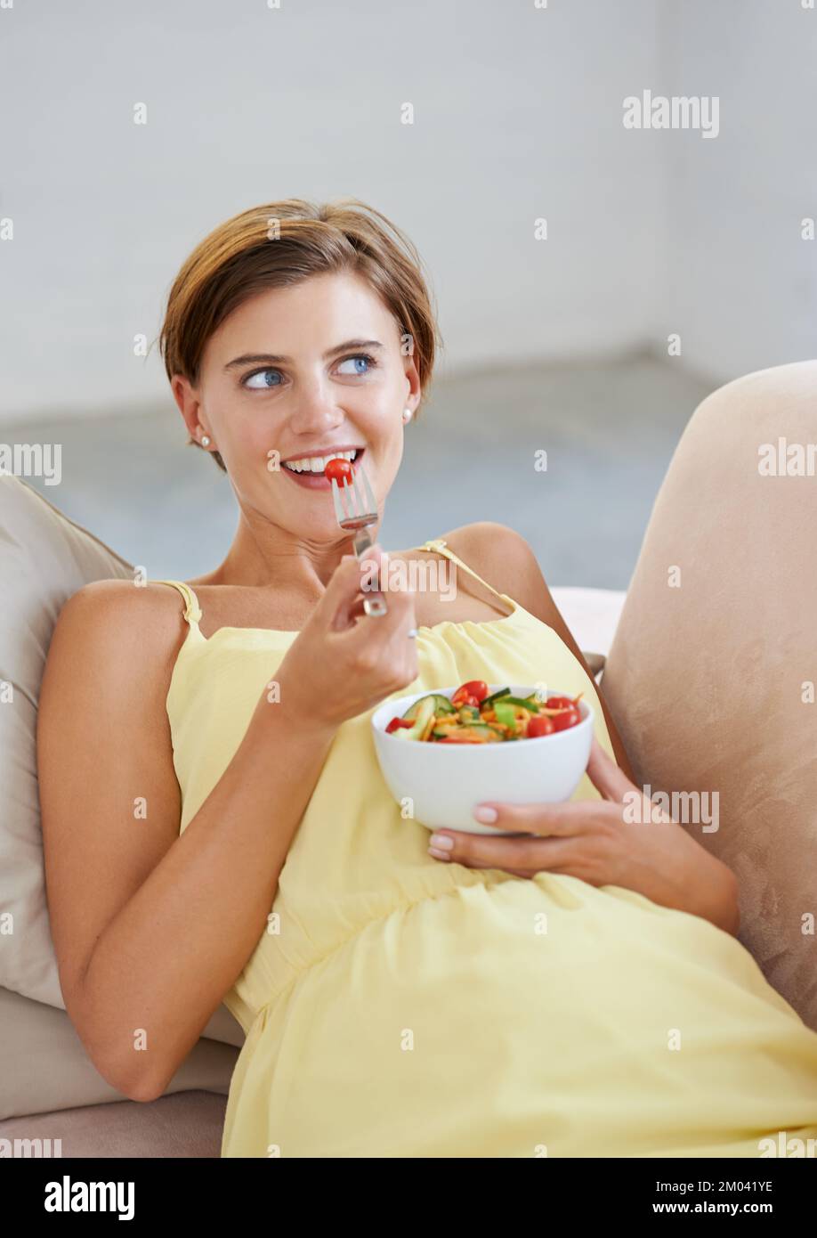 Faire un choix sain. une belle femme enceinte se détendant sur le canapé tout en mangeant une salade fraîche. Banque D'Images