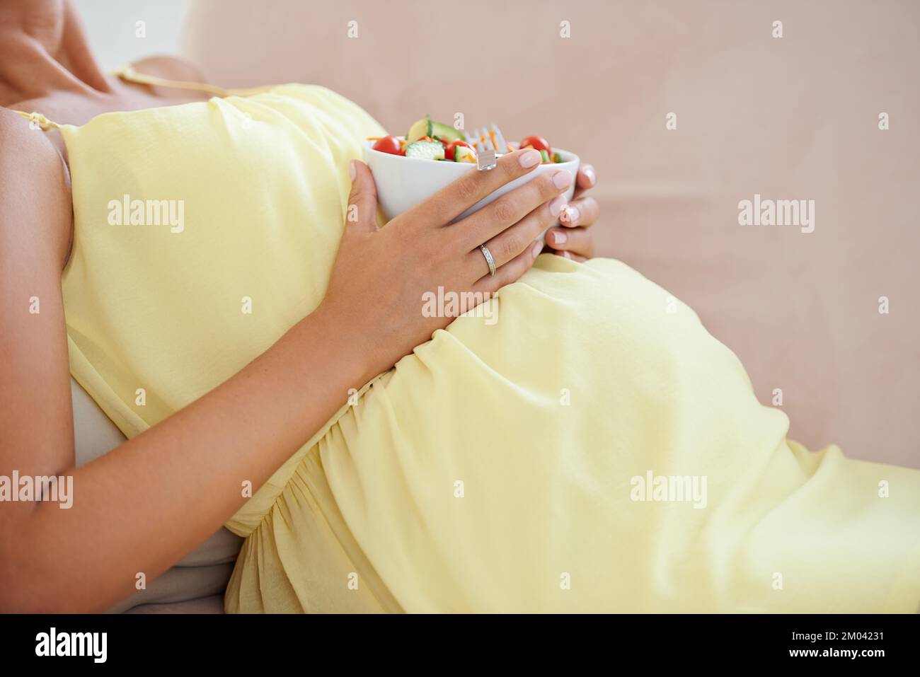 La santé de votre grossesse est entre vos mains. une femme enceinte se détendant sur le canapé tout en mangeant une salade fraîche. Banque D'Images