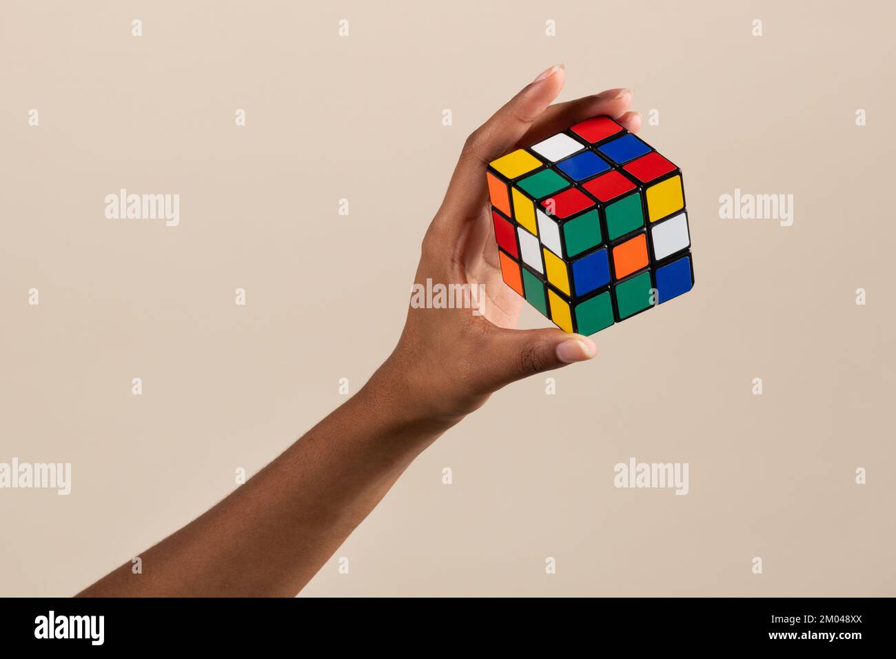 Crop main de la femme noire démontrant un teaser de cerveau non résolu de Rubik cube sur fond beige Banque D'Images