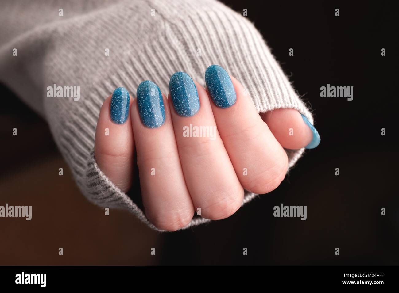 Femme main en tricot gris avec belle manucure - ongles à paillettes bleues. Concept de soin des ongles Banque D'Images