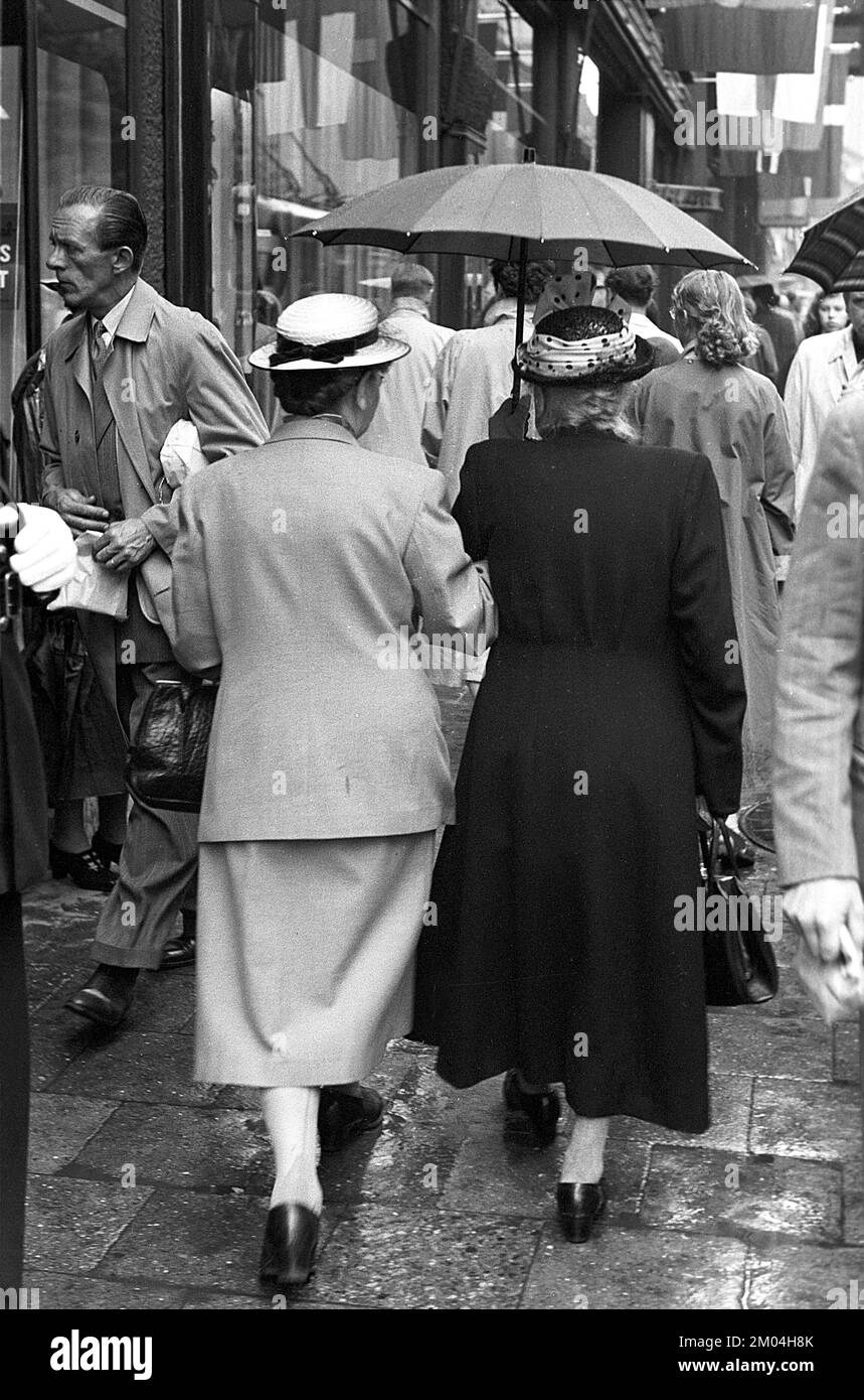 Parasols dans le 1950s. La pluie coule et deux femmes âgées sont vues tenant un parapluie sur elles-mêmes tout en marchant à la tête. C'est un jour pluvieux à Stockholm Suède 1953. réf. 1,2 Banque D'Images