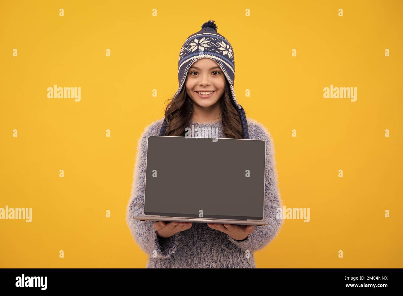 École d'automne. Adolescente fille d'école dans les vêtements d'automne tenir ordinateur portable sur fond jaune isolé de studio. Visage heureux, émotions positives et souriantes de Banque D'Images