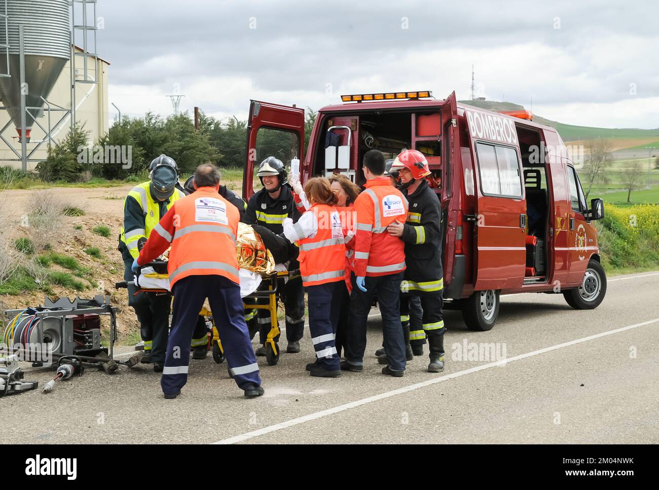 Une fourgonnette de pompiers avec des pompiers, des ambulanciers paramédicaux et des gardes civils qui soignent et encouragent une personne blessée dans un accident de la route. Banque D'Images