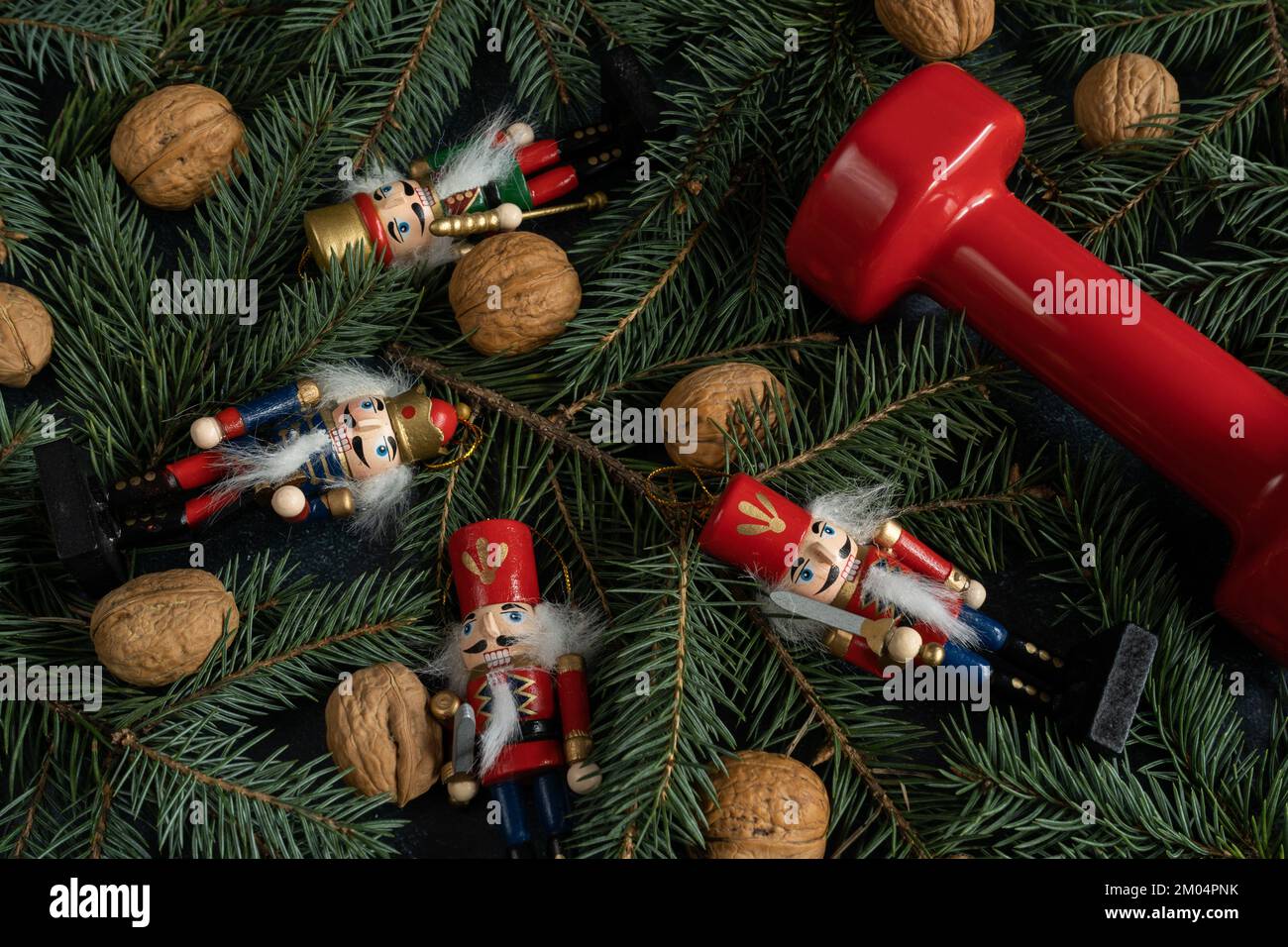 Haltères de gym, figurines de Noël et noix de Grenoble sur les branches des arbres. Saison des fêtes de remise en forme, composition d'entraînement d'hiver. Banque D'Images