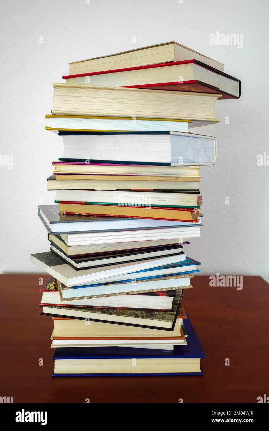 Une pile de livres de formes et d'épaisseurs différentes sur une étagère en bois et un mur blanc en arrière-plan Banque D'Images