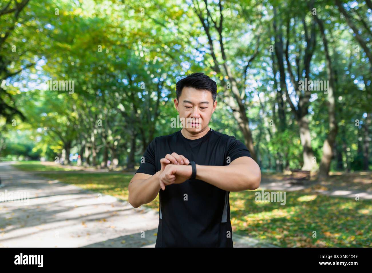 Mode de vie actif, technologies modernes. Un jeune homme asiatique sportif utilise un bracelet de fitness, regarde une montre intelligente tout en faisant du jogging à l'extérieur du parc. Mesure la fréquence cardiaque, le nombre de pas, la distance. Banque D'Images