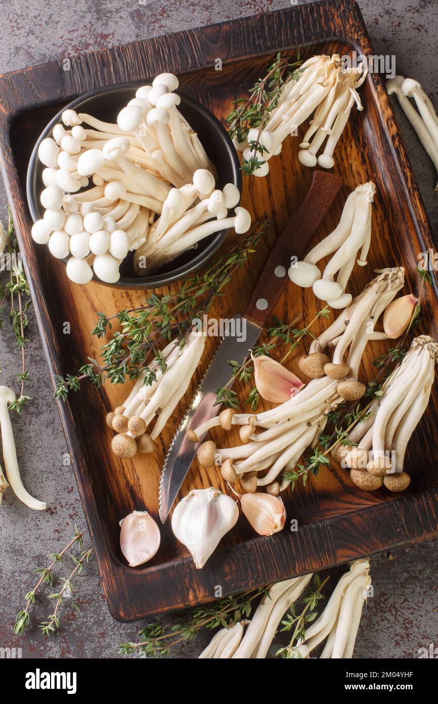 Champignons shimeji frais blancs et bruns comestibles ou de hêtre avec des ingrédients de cuisson à proximité sur bois de table. Vue verticale du dessus Banque D'Images