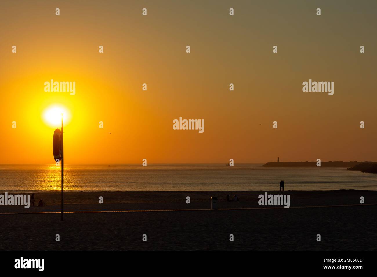 Coucher de soleil sur la plage de Barra, Aveiro, Portugal. Soleil orange et silhouette de bouée de sauvetage et de gens sur la plage. Oiseaux dans le ciel. Banque D'Images