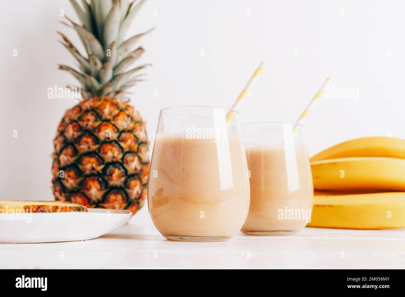 Encore la vie avec des fruits, des bananes, de l'ananas et du smoothie dans des verres sur une table en bois blanc. Concept minimal de diète de détox, boisson de vitamine d'été. Vue avant. Banque D'Images