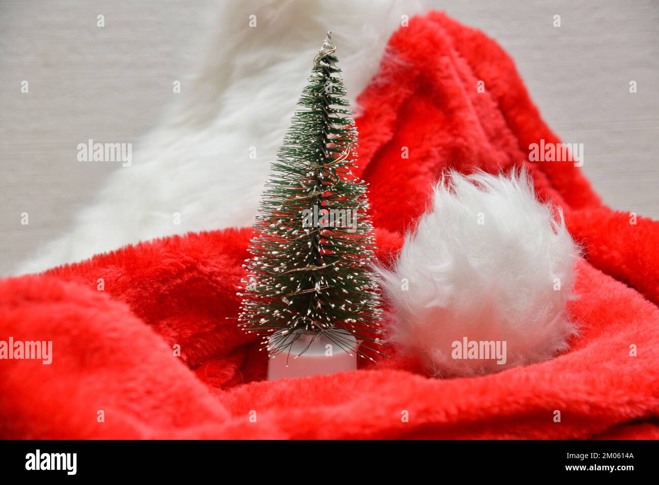 Décorations de Noël. Petit sapin de Noël artificiel recouvert de neige artificielle sur un chapeau rouge du Père Noël. Banque D'Images