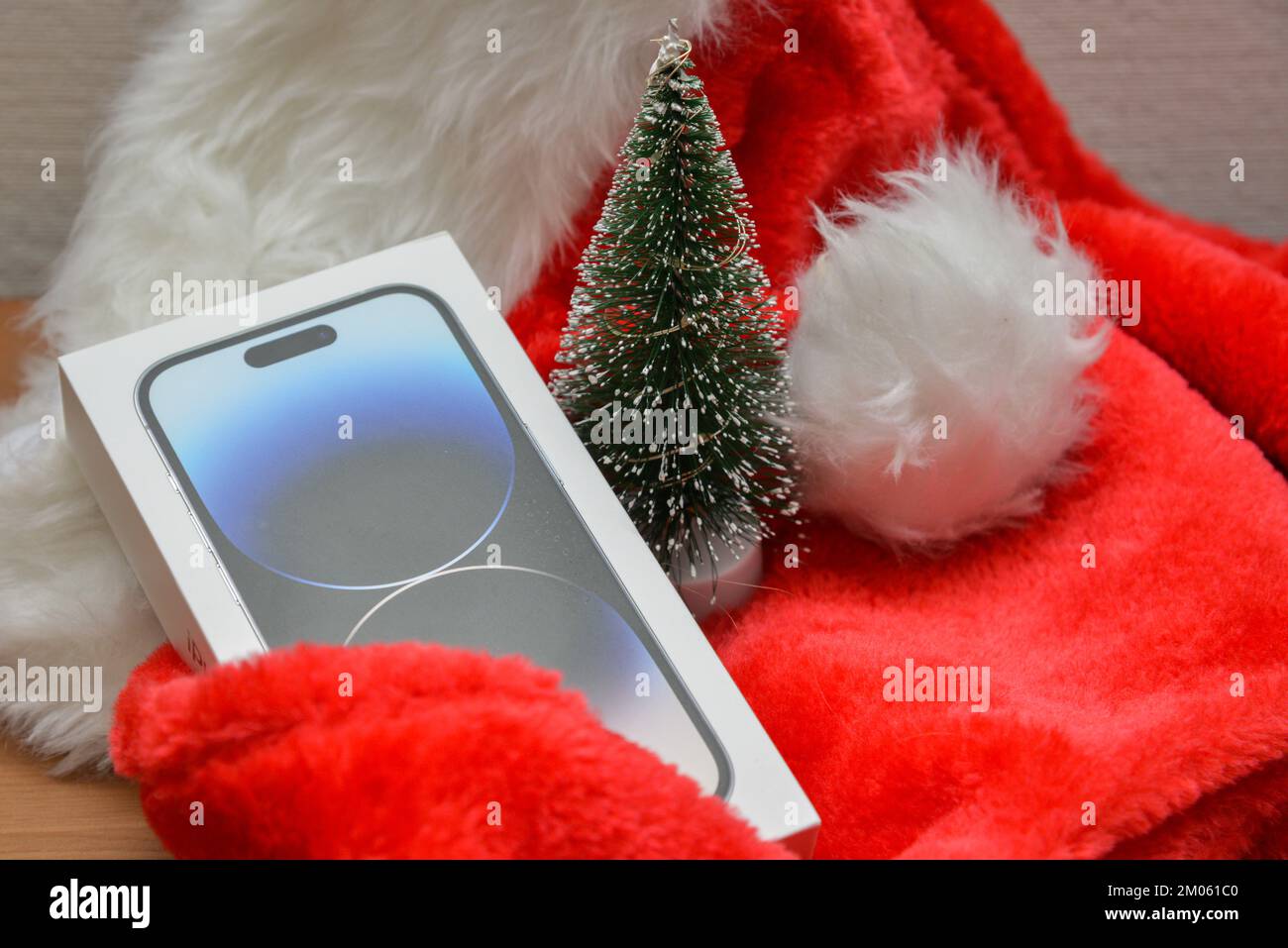 Riga, Lettonie - 4 décembre 2022: Apple iPhone 14 pro smartphone cadeau de Noël sur un chapeau de Père Noël rouge à côté d'un petit vert artificiel de Noël tre Banque D'Images