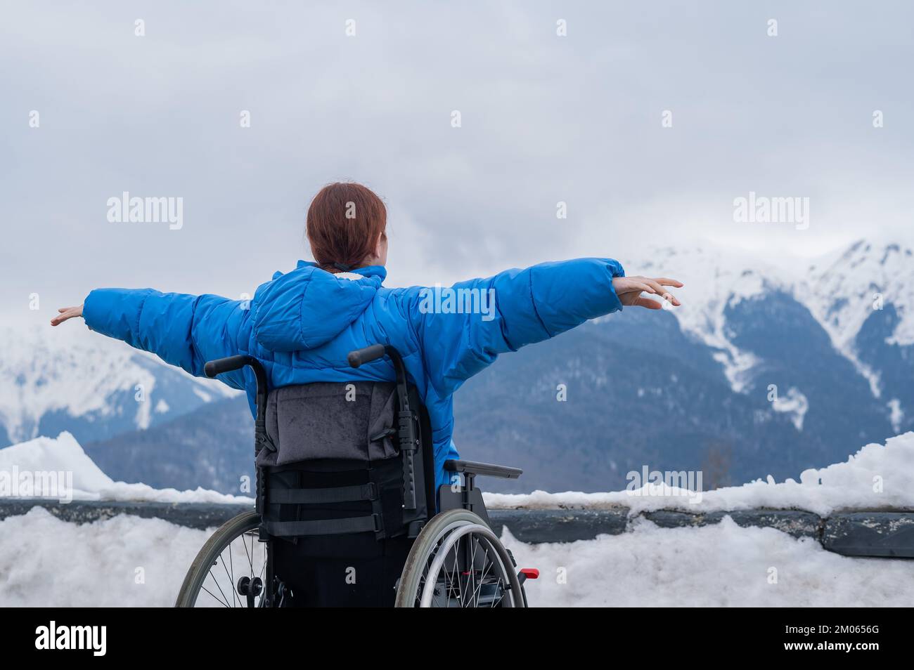 Vue arrière d'une femme en fauteuil roulant, écartez ses bras sur le côté comme des ailes dans les montagnes en hiver. Banque D'Images