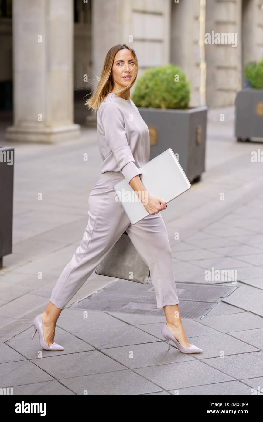 Femme de direction avec ordinateur portable traversant la rue près du bâtiment Banque D'Images