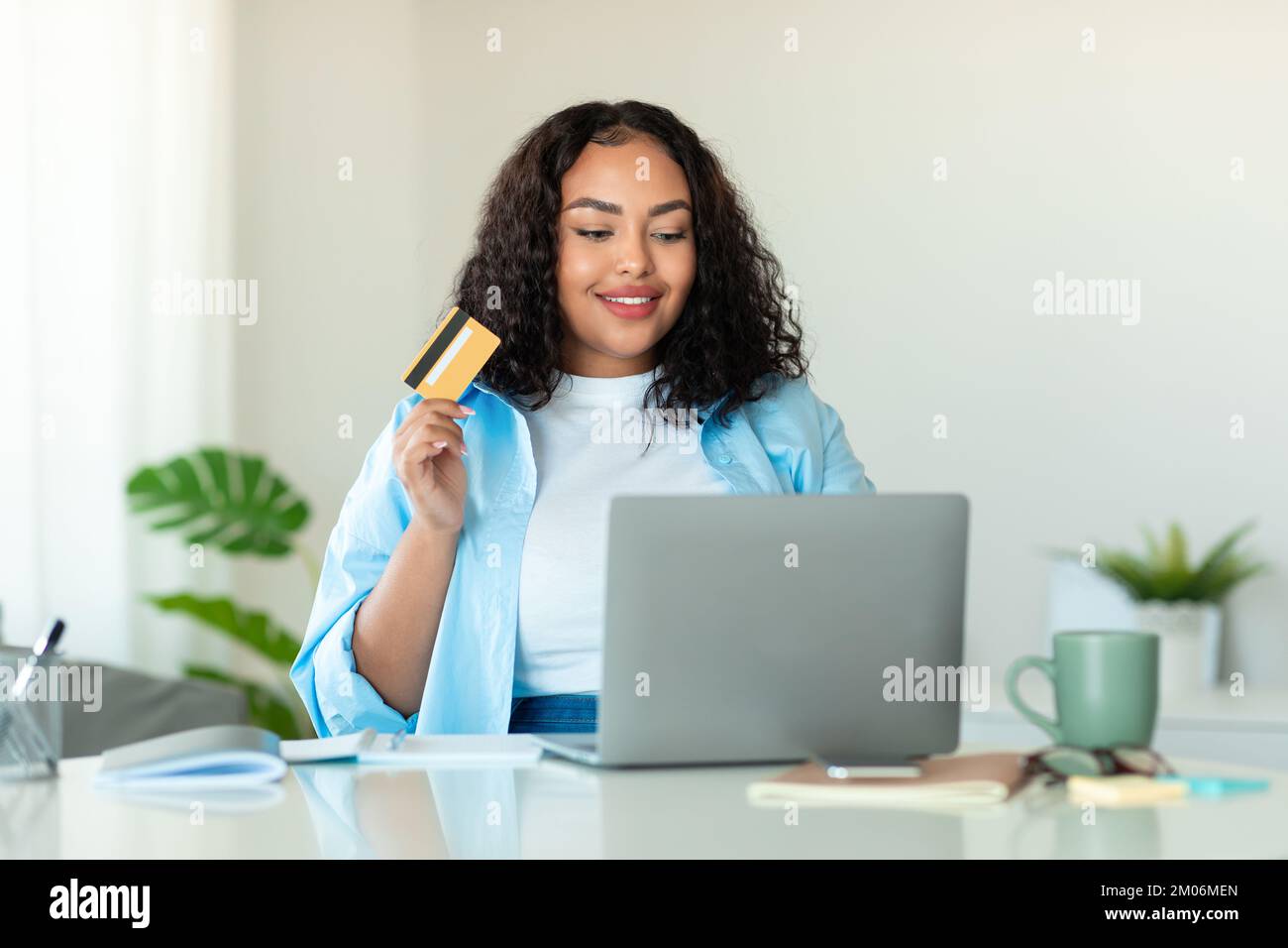 Jeune femme noire surdimensionnée avec carte de crédit en utilisant l'ordinateur portable à la maison, commander de la nourriture ou des achats en ligne, copier l'espace Banque D'Images