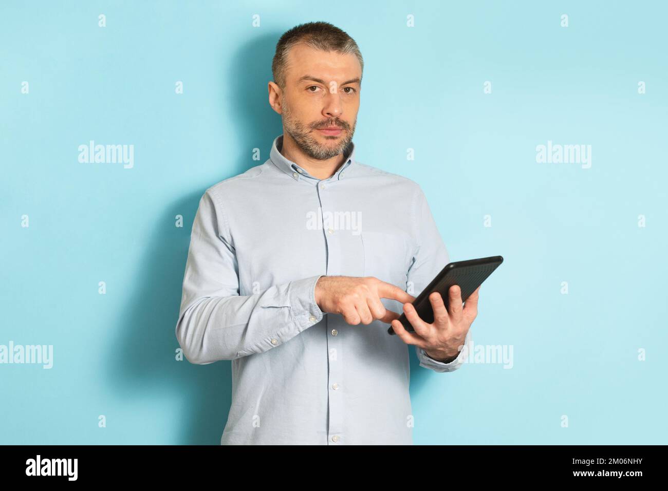 Homme caucasien d'âge moyen sérieux utilisant un ordinateur tablette, debout sur fond bleu studio Banque D'Images