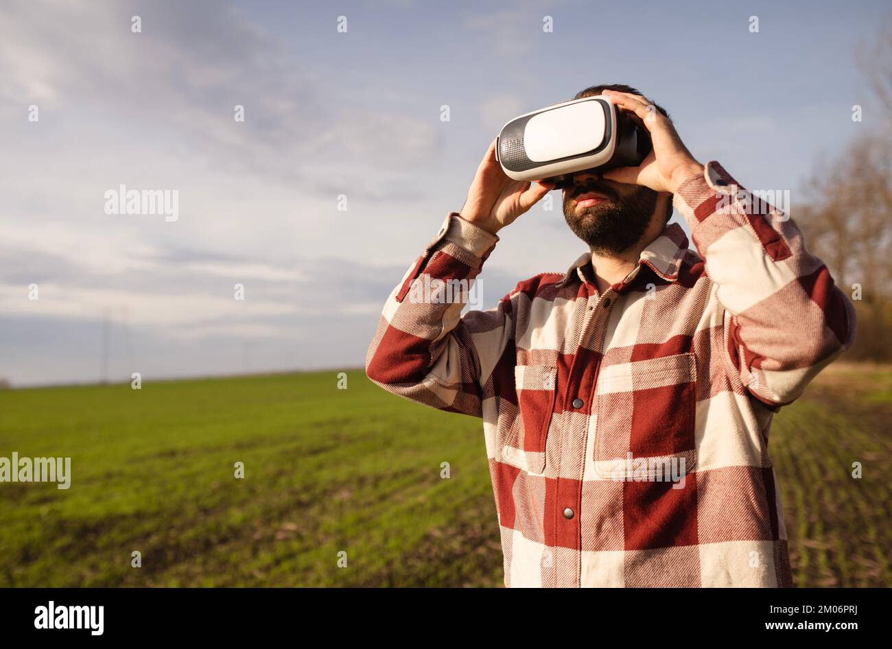 Jeune homme debout dans un champ de blé au coucher du soleil dans des lunettes de réalité virtuelle Banque D'Images