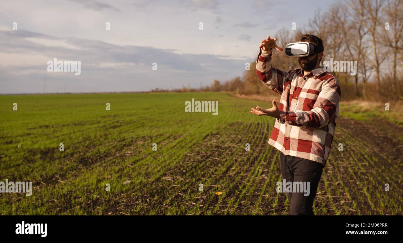 Jeune homme debout dans un champ de blé au coucher du soleil dans des lunettes de réalité virtuelle Banque D'Images