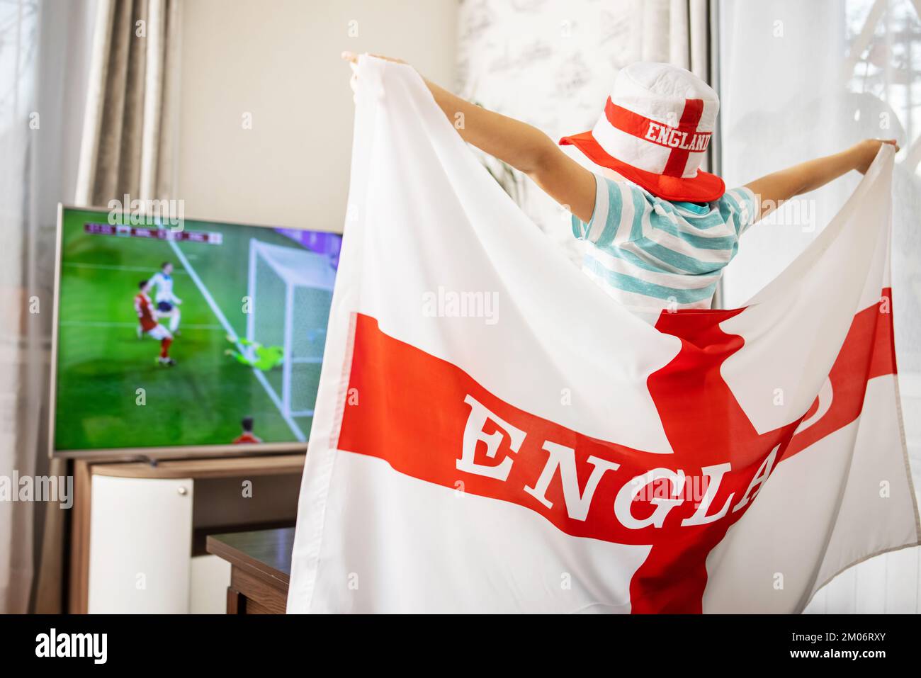 Un garçon tenant le drapeau de l'Angleterre et regardant un match de football à la télévision à la maison Banque D'Images