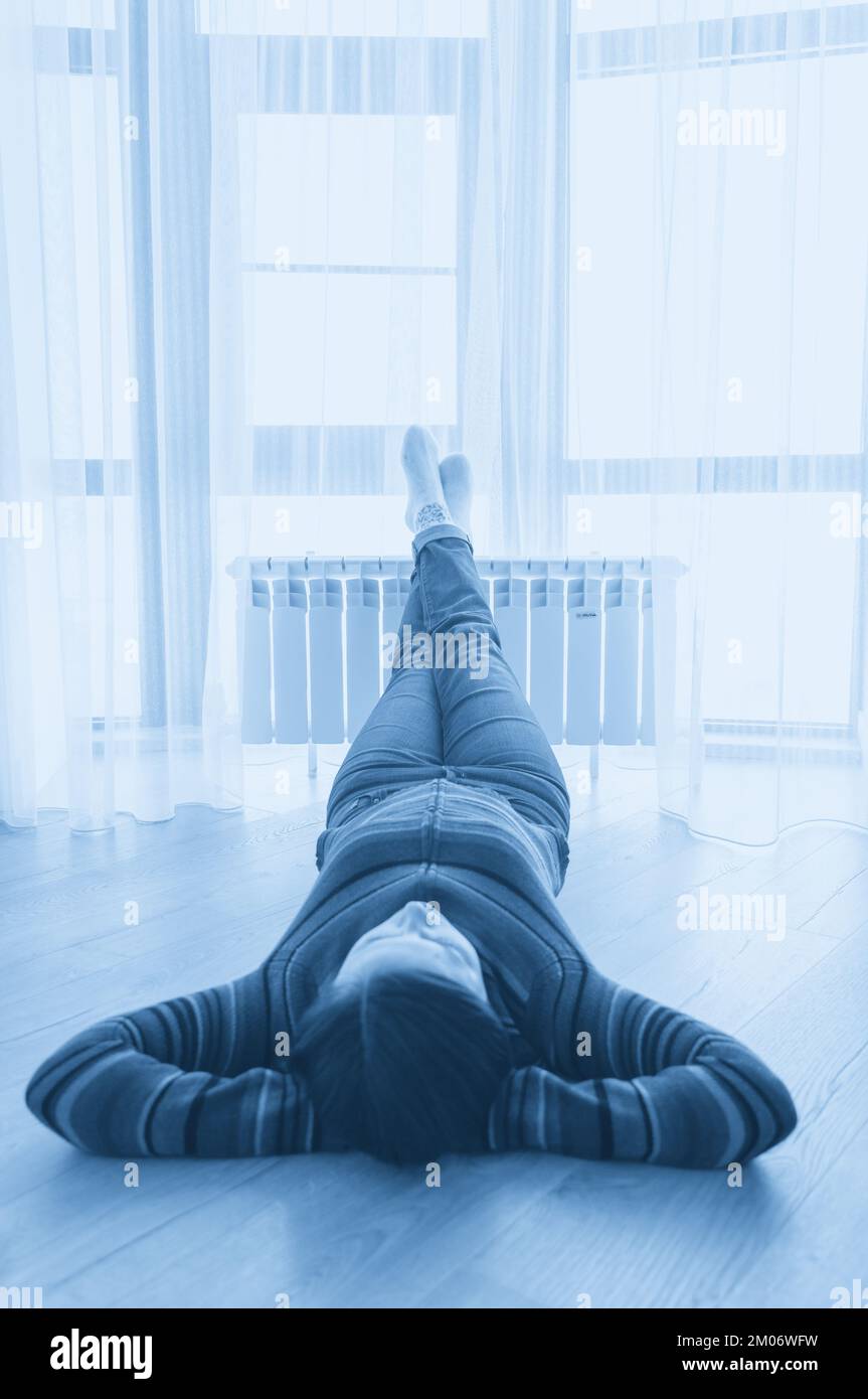 Femme posée sur le sol avec les pieds relevés sur le radiateur pour se réchauffer Banque D'Images