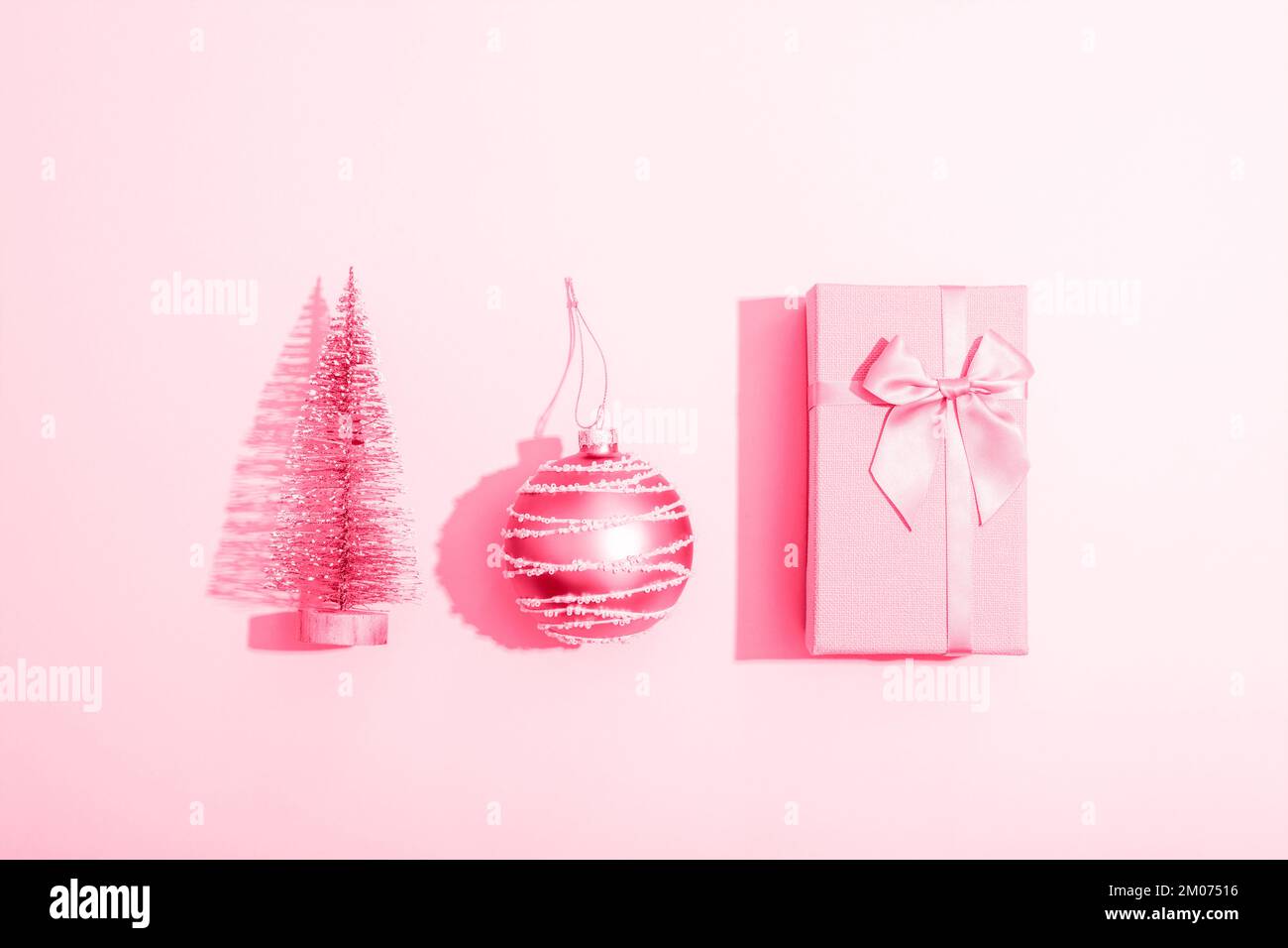 Boîte cadeau, boule de Noël et jouet sapin sur fond rose avec des ombres vives. Composition minimale. Vue de dessus, plan d'agencement. Banque D'Images