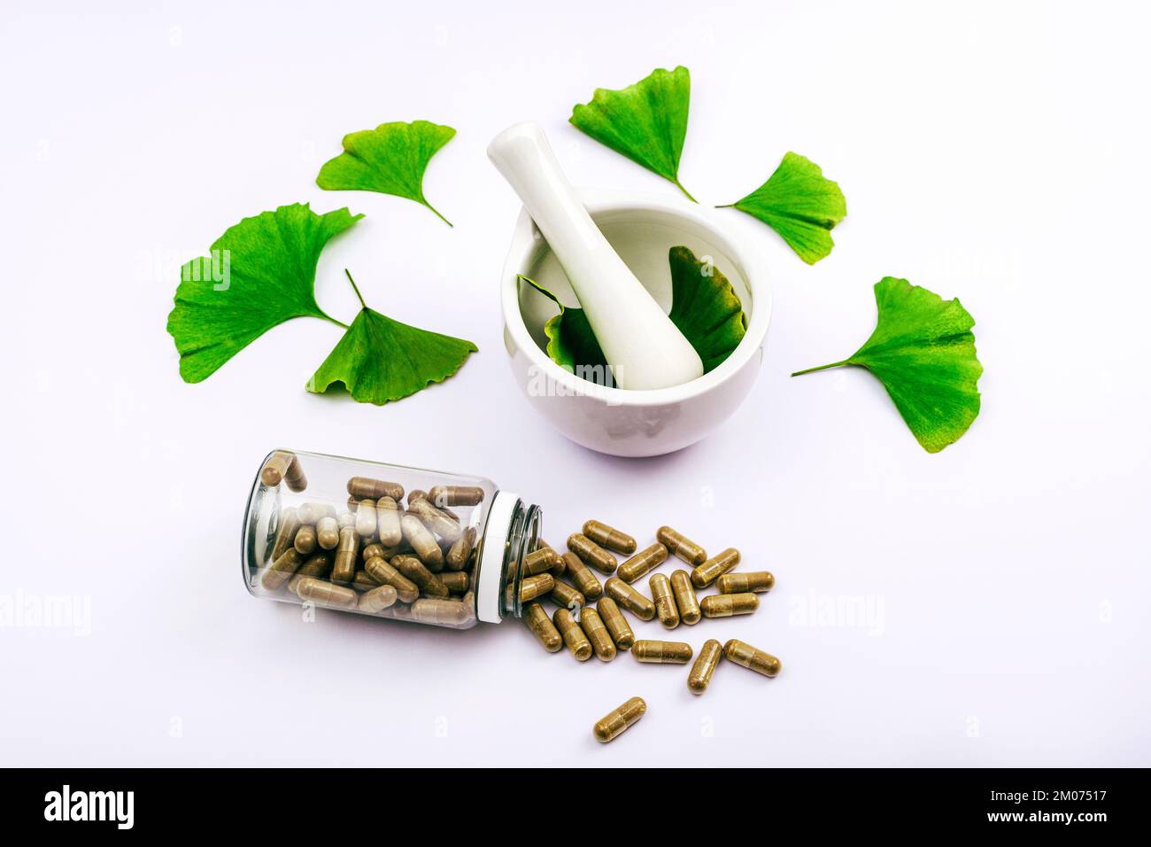 Pilules et feuilles de ginkgo biloba vert frais, mortier et pilon sur fond blanc. Concept de médecine naturelle à base de plantes. Vue de dessus. Banque D'Images