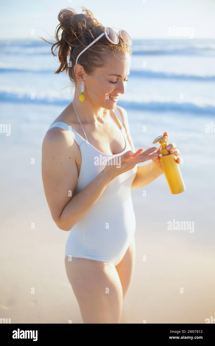 bonne élégante femme d'âge moyen en maillot de bain blanc avec spf à la plage. Banque D'Images