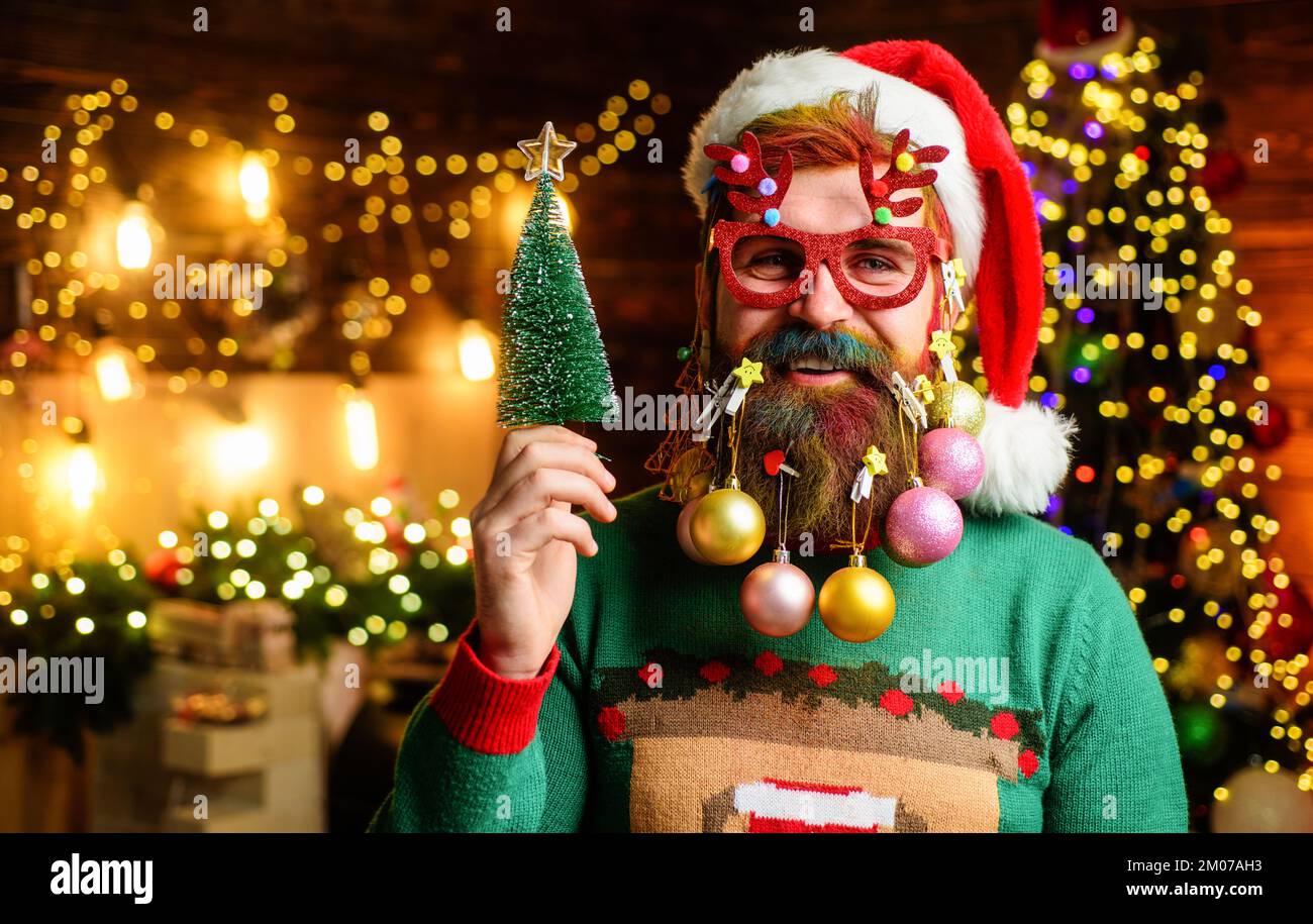 Père Noël en verres de fête avec petit arbre de Noël. Joyeux homme avec des boules de décoration dans la barbe. Banque D'Images
