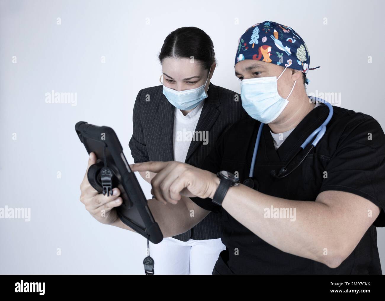 Médecin montrant une tablette à son patient tous deux portant des masques, montrant ou expliquant le contenu qu'il montre. Banque D'Images