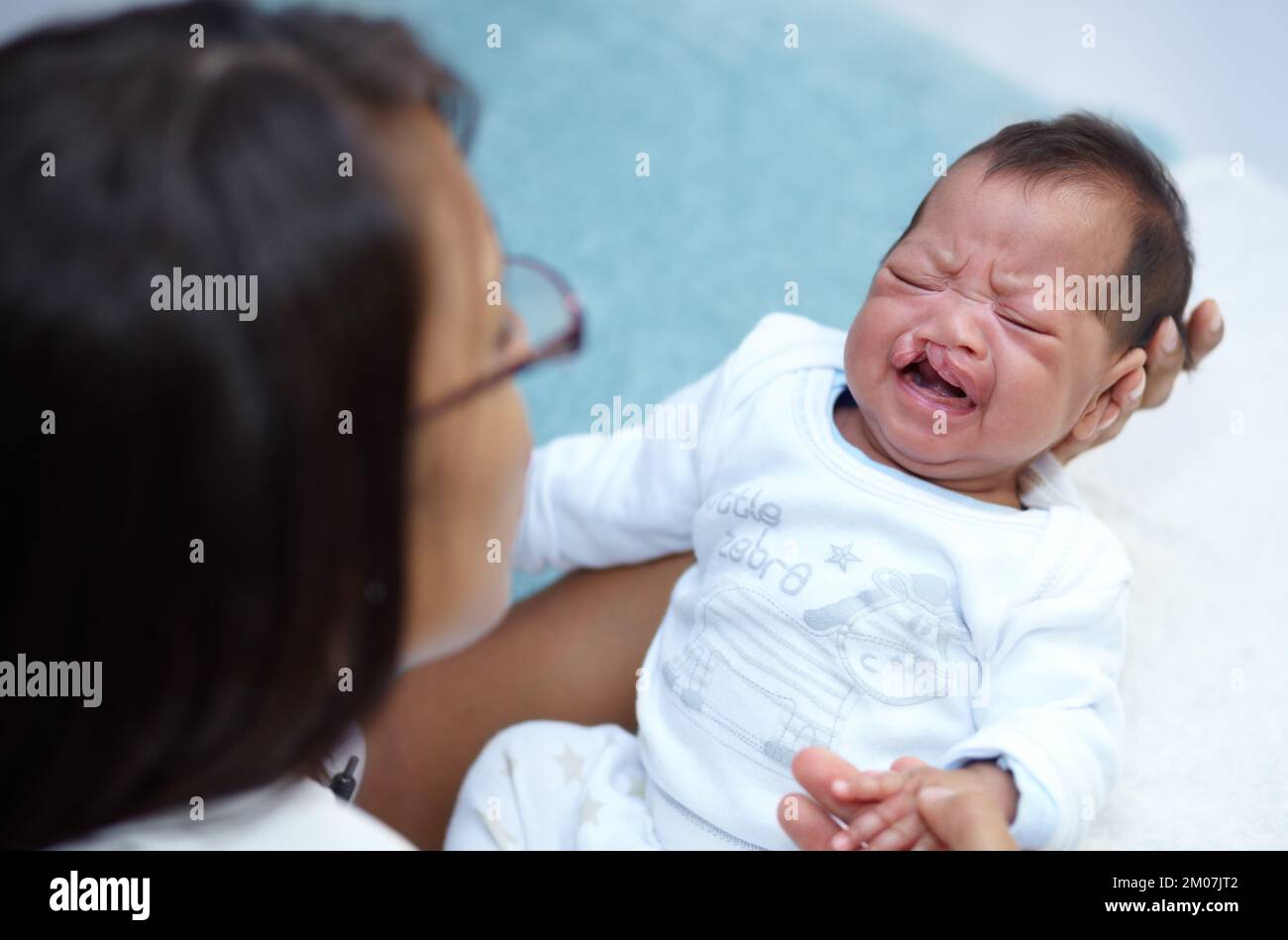 Recherche de confort. Une jeune mère tenant son bébé pleurant qui a un palais de fente. Banque D'Images