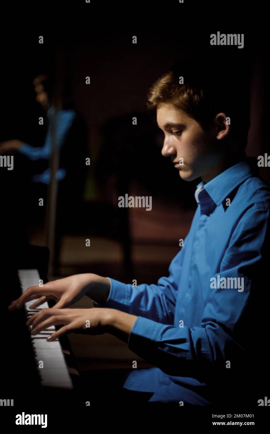 jeune homme assis au piano. garçon joue émotionnellement l'instrument de  clavier dans l'école de musique. l'étudiant apprend à jouer. mains pianiste.  noir foncé b Photo Stock - Alamy