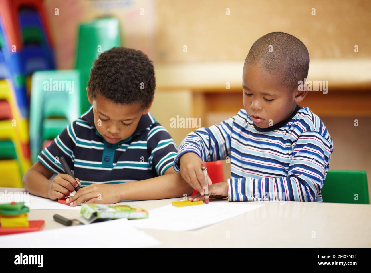 Travailler ensemble sur leur créativité. Deux garçons afro-américains d'âge préscolaire se concentrant sur leurs dessins avec leurs crayons et leurs formes. Banque D'Images