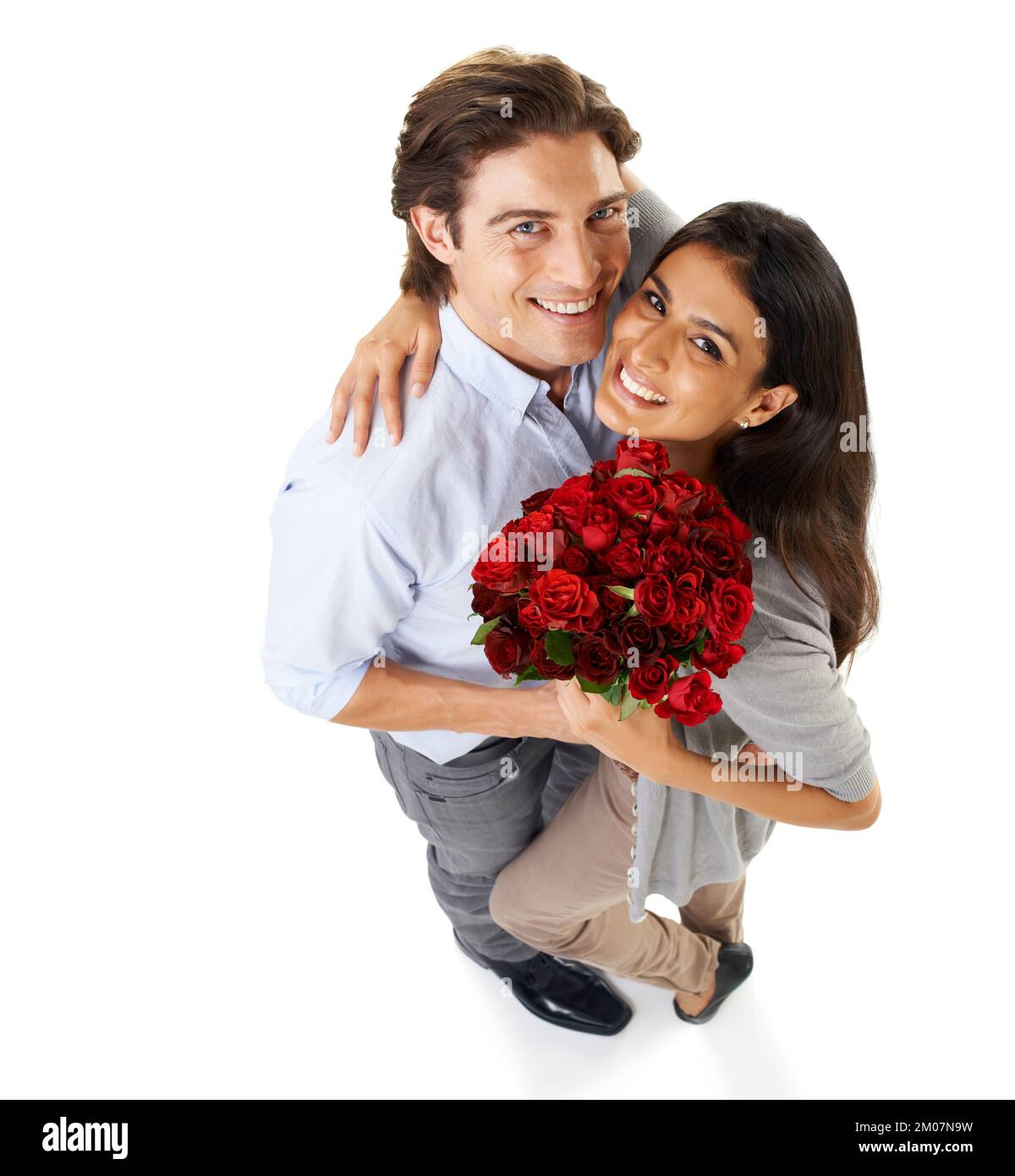 Heureux anniversaire. Portrait en studio grand angle d'un jeune couple embrassant tout en tenant un bouquet de roses isolées sur blanc. Banque D'Images