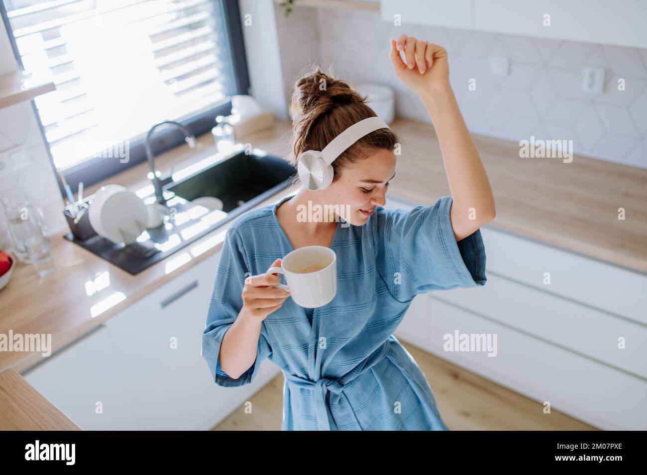 Jeune femme écoutant de la musique et prenant une tasse de café le matin, dans sa cuisine. Banque D'Images